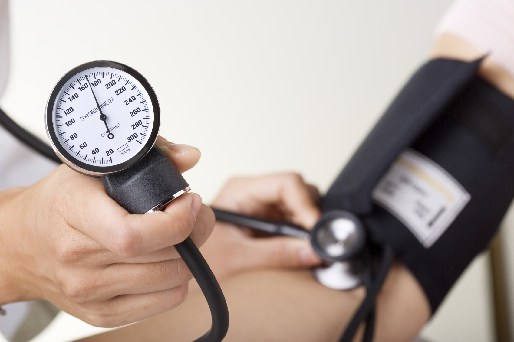 Doctor/nurse checking blood pressure with sphygmomanometer gauge in focus.